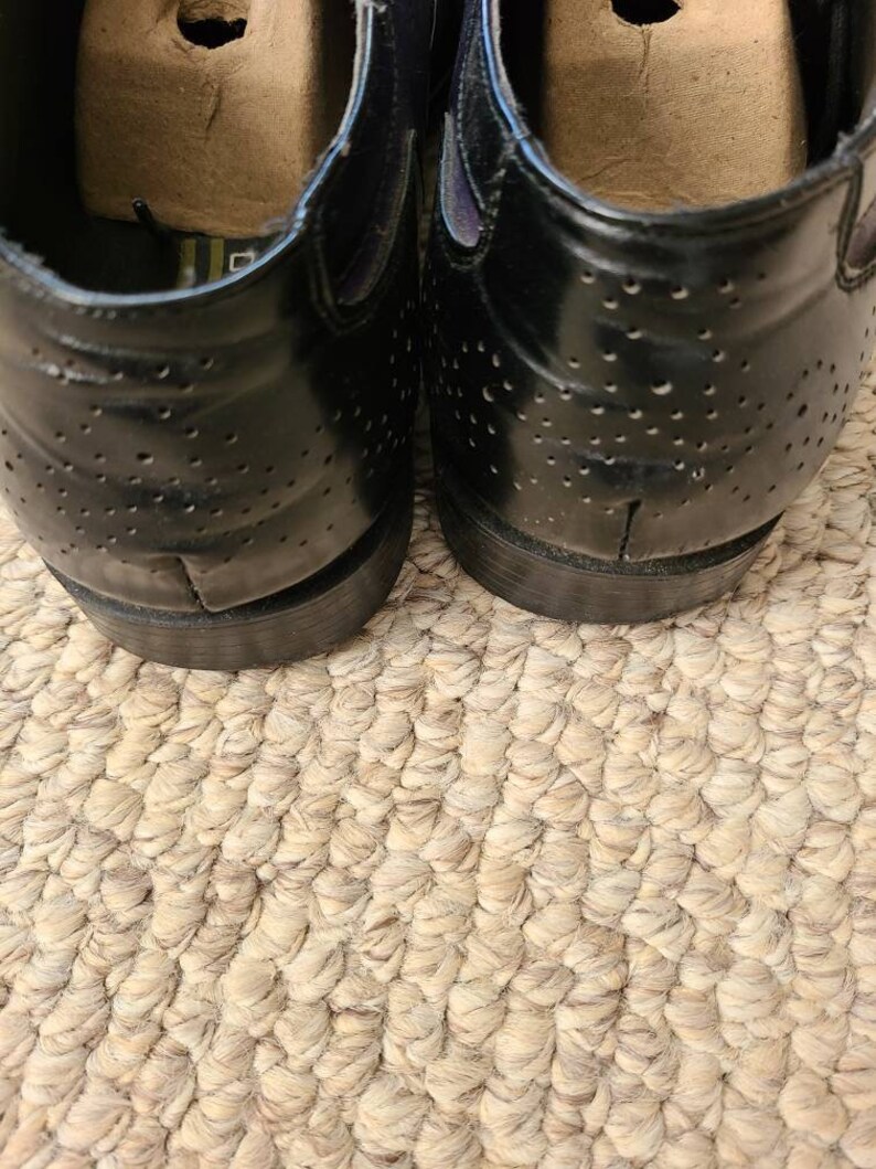 May include: A pair of black leather shoes with a perforated design. The shoes have a rounded toe and a low heel.