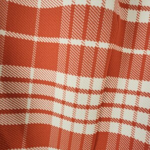 May include: A close-up of a red and white plaid fabric. The fabric has a woven texture and a subtle sheen.