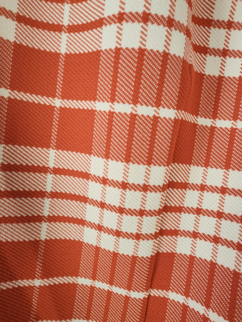 May include: A close-up of a red and white plaid fabric. The fabric has a woven texture and a subtle sheen.