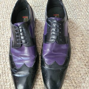 May include: A pair of black and purple leather dress shoes with lace-up closures. The shoes have a wingtip design and a brogue pattern.