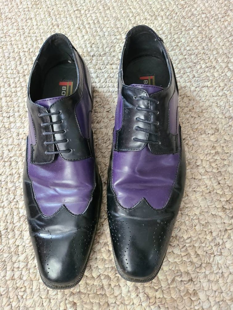 May include: A pair of black and purple leather dress shoes with lace-up closures. The shoes have a wingtip design and a brogue pattern.