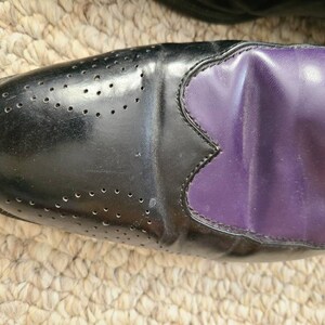 May include: Black leather oxford shoes with a purple leather panel on the toe. The shoes have a brogue design with small holes.
