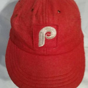 May include: A red baseball cap with a white felt Philadelphia Phillies logo.