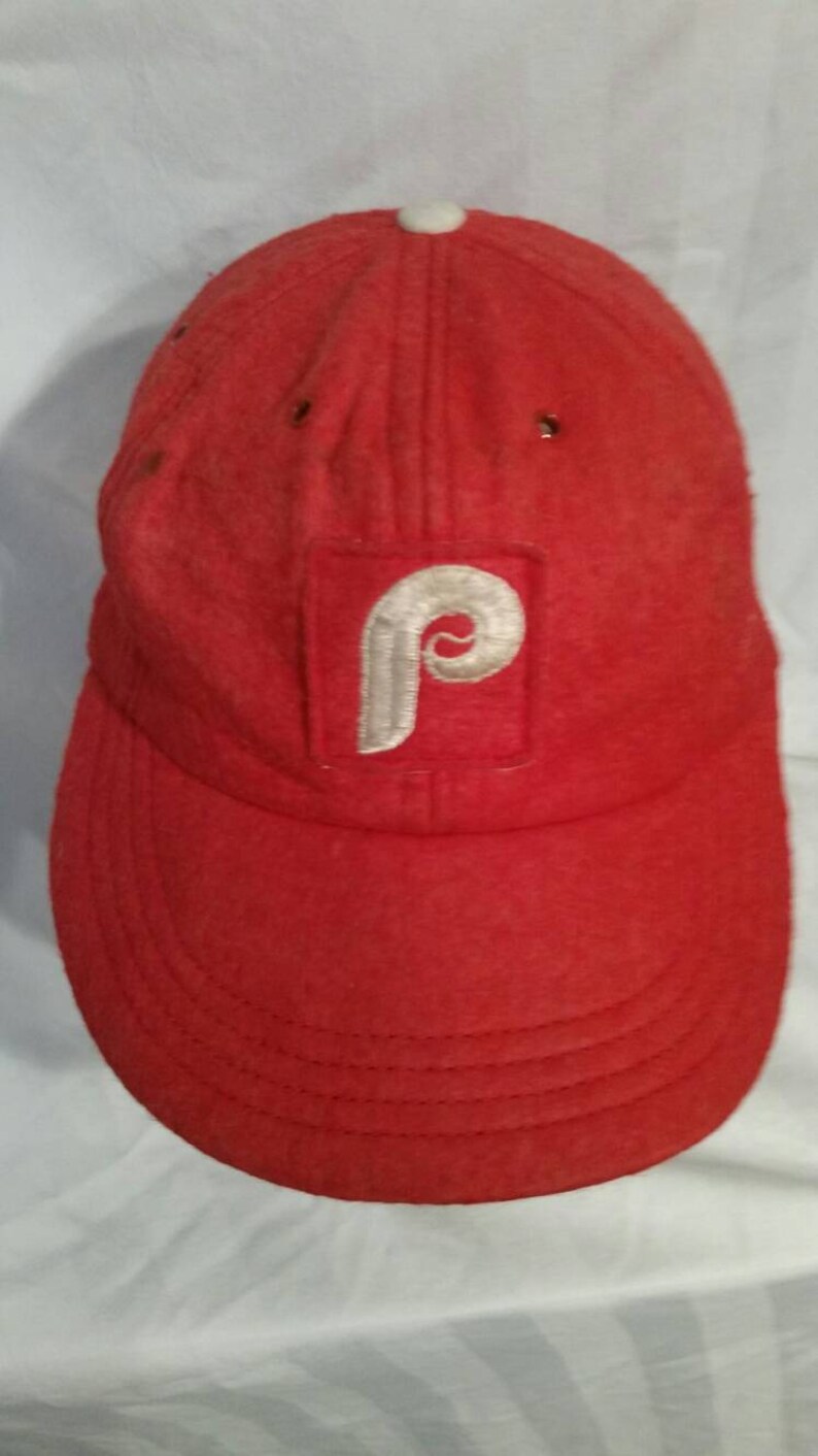 May include: A red baseball cap with a white felt Philadelphia Phillies logo.