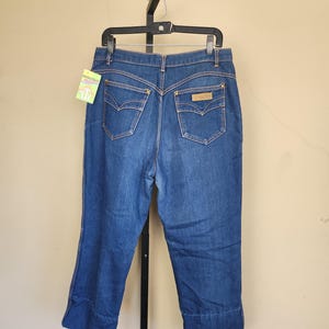 May include: Blue denim jeans with a high waist and flared leg. The jeans have decorative stitching, back pockets, and a small label. The jeans are hanging on a black hanger.