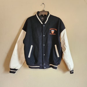May include: A black and white varsity jacket with a white leather sleeve. The jacket has a Princeton University logo on the chest.
