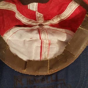 May include: Red and blue baseball cap with a brown leather band. The inside of the cap is white with red stitching. The cap has the text "FT. WORTH 1947 FIRE DEPT." written in black ink on the inside.