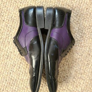 May include: A pair of black and purple leather dress shoes with brogue detailing. The shoes have a lace-up closure and a pointed toe.