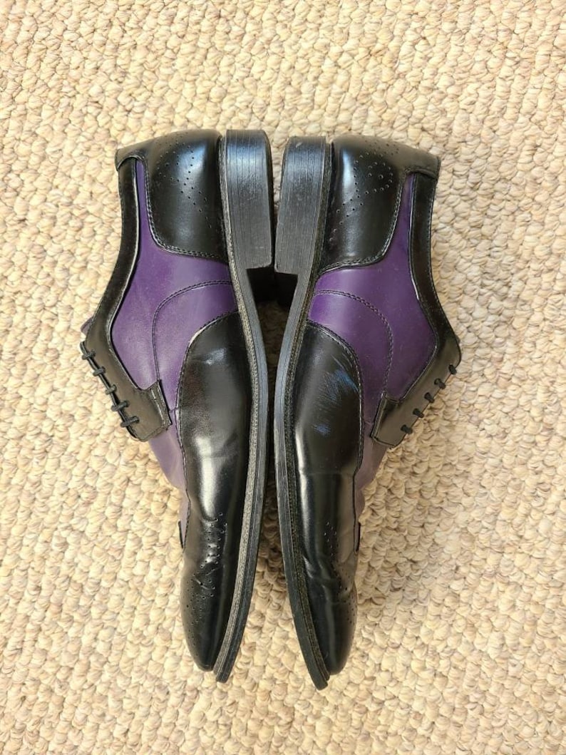 May include: A pair of black and purple leather dress shoes with brogue detailing. The shoes have a lace-up closure and a pointed toe.