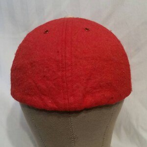 May include: Red wool baseball cap with a white brim. The cap is on a gray mannequin head.