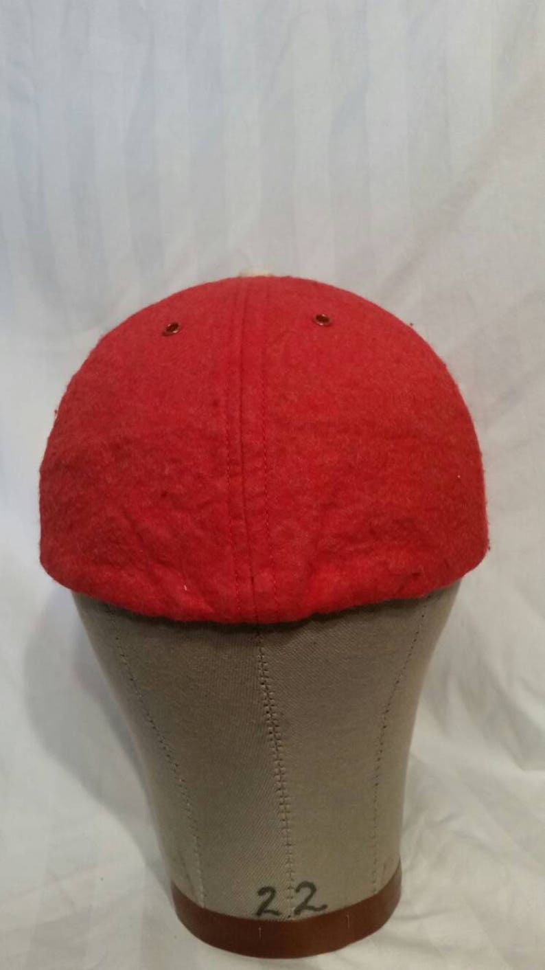 May include: Red wool baseball cap with a white brim. The cap is on a gray mannequin head.