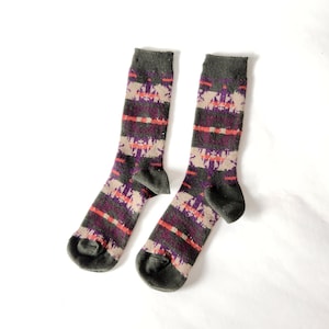 May include: A pair of green, purple, and orange patterned socks. The socks are made of a soft, comfortable material and have a ribbed texture.