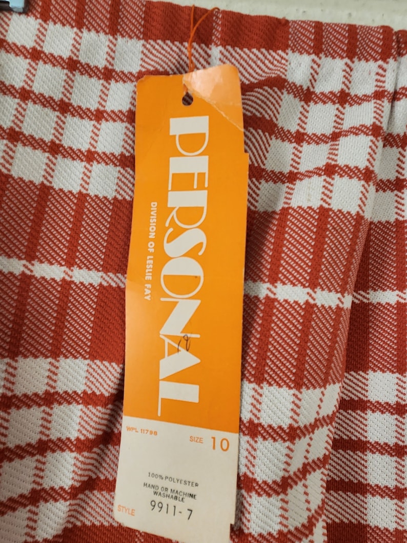 May include: Orange and white tag with the text "PERSONAL" and "DIVISION OF LESLIE FAY" in black. The tag also includes the text "WPL 11798", "SIZE 10", "100% POLYESTER", "HAND OR MACHINE WASHABLE", "9911-7", and "STYLE".