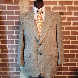 May include: A tweed blazer in shades of gray and brown, paired with a paisley patterned tie in red, yellow, and orange. The jacket has two front pockets and a two-button closure. The outfit is displayed on a mannequin.