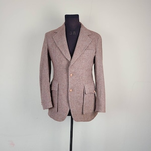 May include: A brown tweed blazer with a single-breasted closure and two flap pockets. The blazer has three copper-colored buttons.