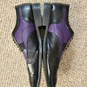 May include: A pair of black leather dress shoes with purple accents. The shoes have a lace-up closure and a pointed toe.