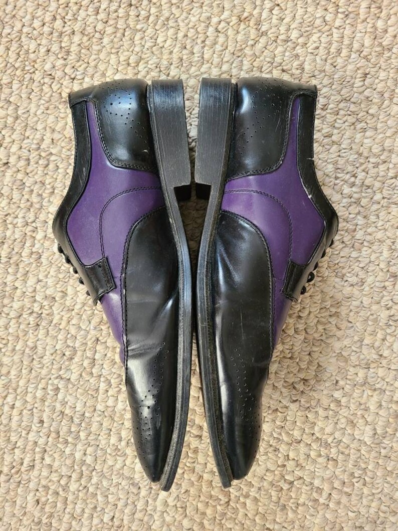 May include: A pair of black leather dress shoes with purple accents. The shoes have a lace-up closure and a pointed toe.