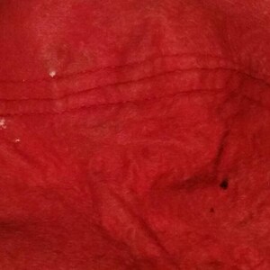 May include: Close-up of a red fabric surface with visible stitching and a few white spots.