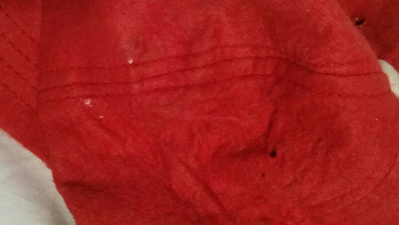 May include: Close-up of a red fabric surface with visible stitching and a few white spots.