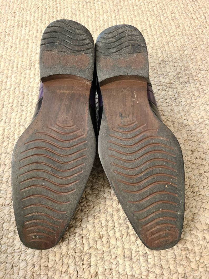 May include: A pair of black leather shoes with purple accents. The shoes have a wavy pattern on the soles.