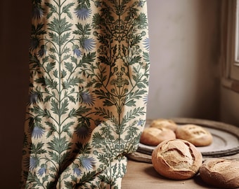 May include: A beige curtain featuring a repeating pattern of green leaves and blue flowers. Several round loaves of bread sit on a wooden tray on a wooden surface, next to the curtain.