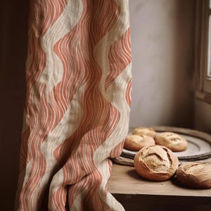 Può includere: Una tenda beige e corallo con un motivo a righe ondulate è appesa accanto a un tavolo di legno. Diversi panini rotondi e croccanti sono sul tavolo e un piatto decorativo. La tenda è realizzata in tessuto strutturato.