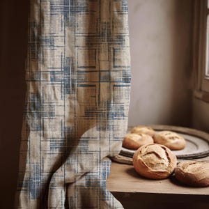 Può includere: Una tenda beige e blu a fantasia è appesa accanto a un tavolo di legno. Diverse pagnotte di pane rotonde sono appoggiate sul tavolo e un vassoio di legno. La tenda ha un design a griglia con toni blu e beige.