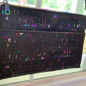 May include: A black crossbody bag with a zipper closure and a colorful confetti pattern. The bag has a long adjustable strap and a small pocket on the front.