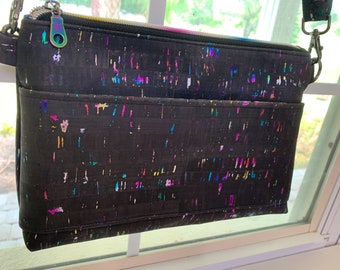 May include: A black crossbody bag with a zipper closure and a colorful confetti pattern. The bag has a long adjustable strap and a small pocket on the front.