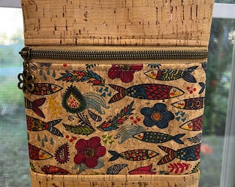 May include: A cork and fabric crossbody bag with a zippered pocket and a colorful fish and floral print. The bag has a brown cork strap.