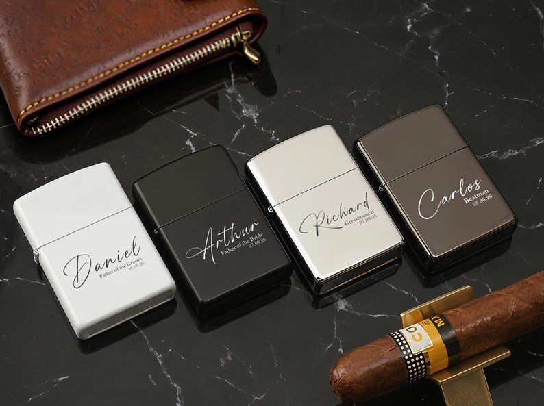 May include: Four personalized lighters in white, black, silver, and brown, each engraved with a name and date. A brown leather wallet and a cigar with a gold holder are also visible on a black marble surface.