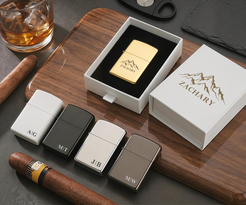 May include: An assortment of personalized lighters in various colors, including gold, black, white, and silver. One gold lighter is displayed in a white box with the name "ZACHARY" and a mountain graphic. Other lighters have initials engraved.