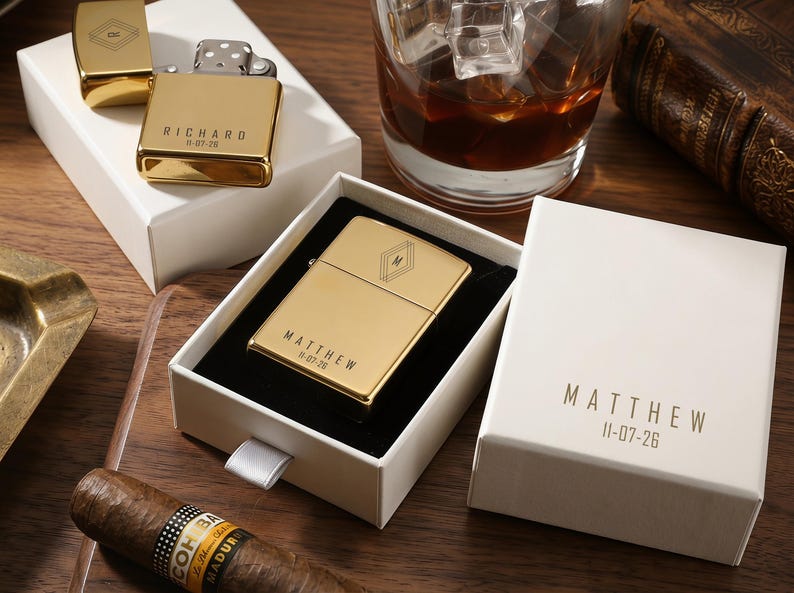 May include: Gold-colored lighters with personalized text and geometric designs are displayed in white boxes. One lighter is open, revealing the flint and wick. A glass of whiskey with ice and a cigar are also visible.