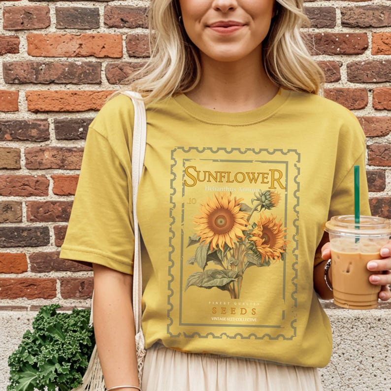 May include: Mustard yellow t-shirt featuring a vintage-style sunflower graphic. The graphic includes the word "Sunflower" at the top, with "Seeds" at the bottom. The design showcases a detailed illustration of sunflowers in full bloom.