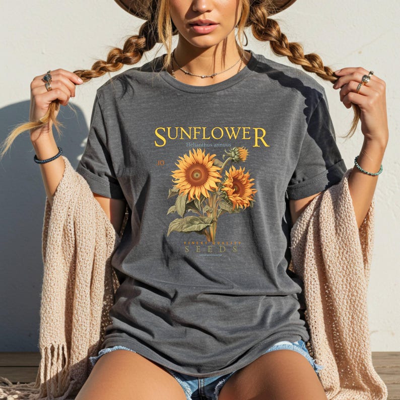 May include: Dark gray t-shirt featuring a botanical illustration of sunflowers with the word "SUNFLOWER" in yellow script. The shirt also includes the text "Helianthus annuus" and "Finest Quality Seeds".