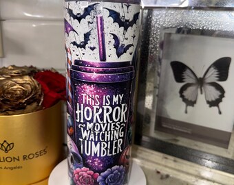 May include: A stainless steel tumbler with a spooky theme. The tumbler features bats, a purple and black galaxy design, and the text "THIS IS MY HORROR MOVIES WATCHING TUMBLER". It includes a silver straw and is decorated with roses and skulls.