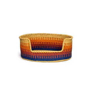 May include: A woven pet bed with a rounded shape and a deep, comfortable interior. The bed is made of natural materials and features a colorful striped pattern in shades of blue, orange, and brown.