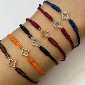 May include: A set of six bracelets with different colored cords and a small diamond clover charm on each. The bracelets are tied with a knot and have a sliding closure.