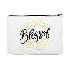 May include: White zippered pouch with a black zipper and a gold sunburst design with the word "Blessed" in black script.