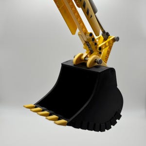 Peut inclure: Un jouet d'excavatrice jaune et noir avec un godet noir. Le godet a une série de dents sur le bord inférieur.