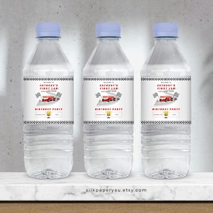 May include: Three clear plastic water bottles with white labels. The labels feature a red race car graphic and the text "Welcome to Anthony's First Lap Around the Track Birthday Party".
