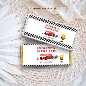 May include: Two printable chocolate bar wrappers featuring a racing car theme. The wrappers are white with black and white chequered borders. The text on the wrappers reads "Anthony's First Lap" with a red race car and the words "Finish" and "Place 1st". The date "October 14th" is also included on the wrappers.