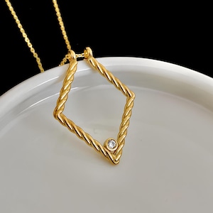 May include: A gold necklace with a diamond-shaped pendant. The pendant is made of twisted gold wire and has a small clear stone in the center.
