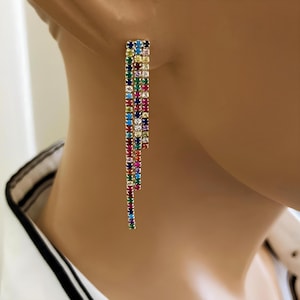 May include: A pair of long, dangling earrings with a cascade of colorful square-shaped gemstones. The earrings are made of gold and feature a rainbow of colors, including red, orange, yellow, green, blue, indigo, and violet.