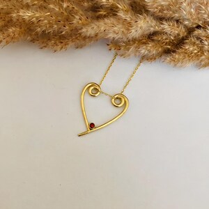May include: A gold heart-shaped necklace with a small red gemstone in the center.