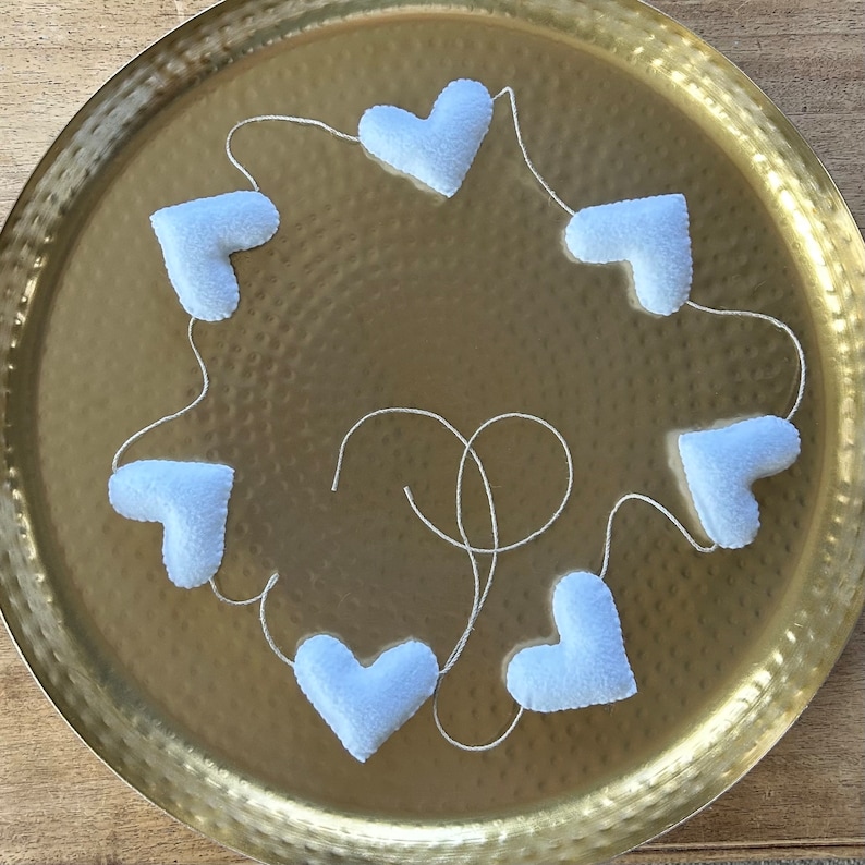 A white felt heart garland with seven hearts strung together on a natural cord.  The garland is displayed on a gold tray.