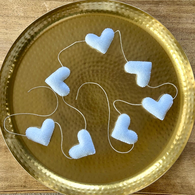 A garland of white felt hearts strung together with natural cord on a gold tray.