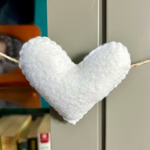 A white felt heart hanging from a string. The heart is fluffy and has a slightly textured surface.