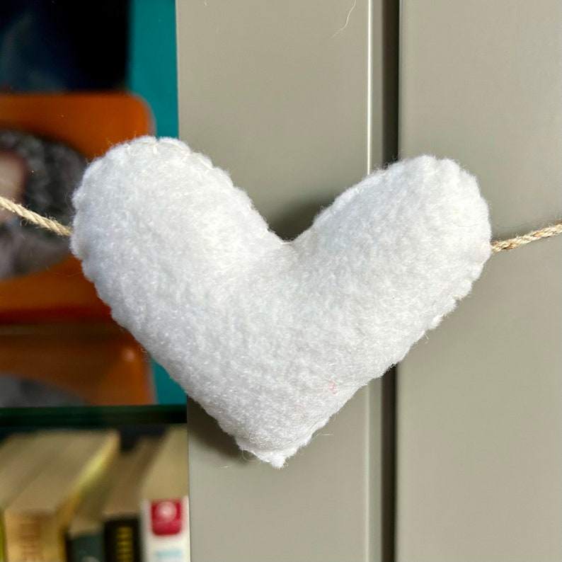 A white felt heart hanging from a string. The heart is fluffy and has a slightly textured surface.