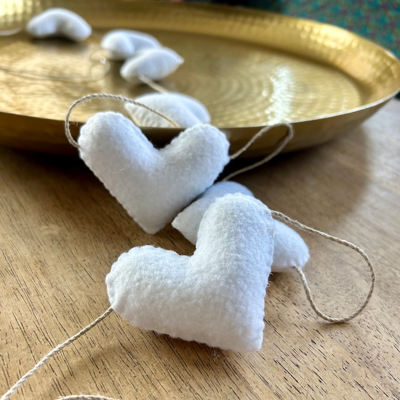 A string of white felt hearts connected with natural cord. The hearts are hanging from a gold tray.